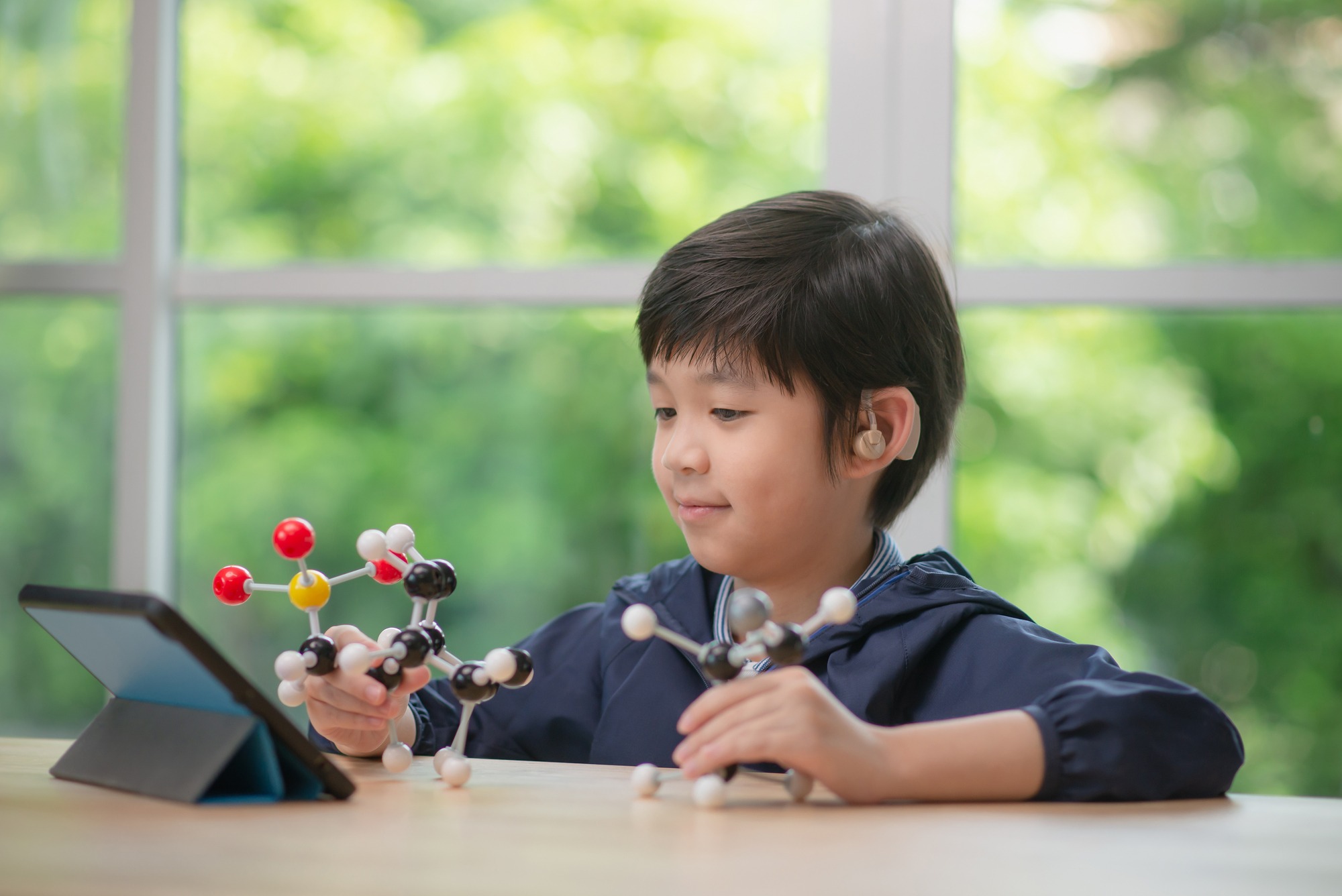 Asian child with hearing aid constructing molecular model in science classroom